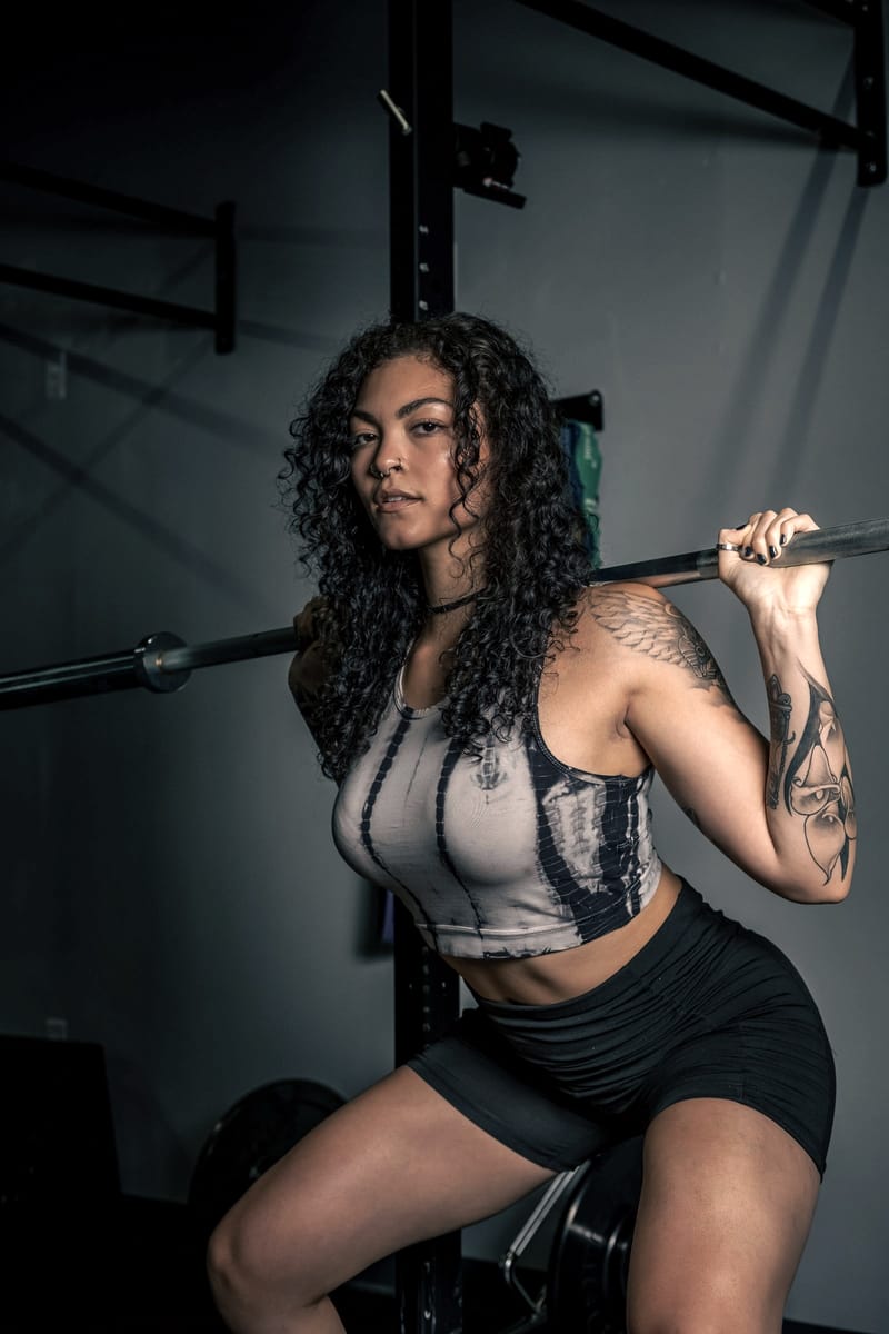 A lifter with a barbell racked across her back in a dimly lit gym